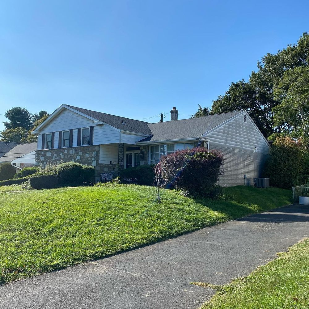 House with asphalt driveway and grassy lawn on a sunny day.