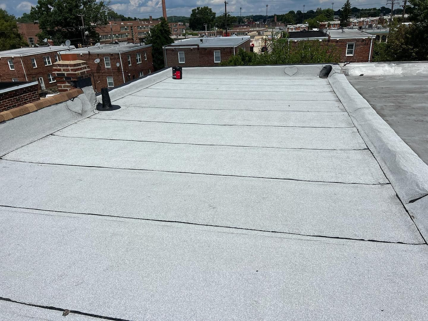 Flat roof with white granules, bordering trim, dotted lines, and a distant cityscape under a bright sky.