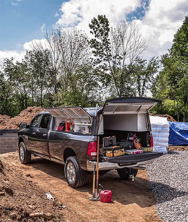Black pickup truck with open tailgate and canopy, parked at a muddy worksite with tools and supplies.