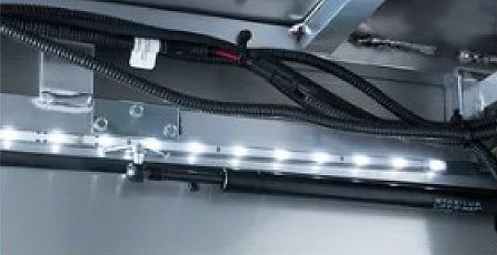 Close-up of black cables and a metal rail inside a gray machine housing, lit by small LED lights