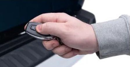 Hand holding a car key fob near a vehicle door handle