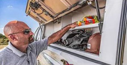 Man reaching into an open storage compartment on a vehicle or aircraft, with tools and gear inside