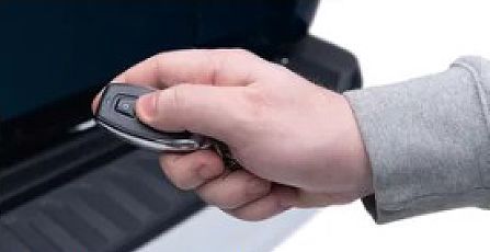 Hand holding a car key fob near a car door handle to unlock the vehicle