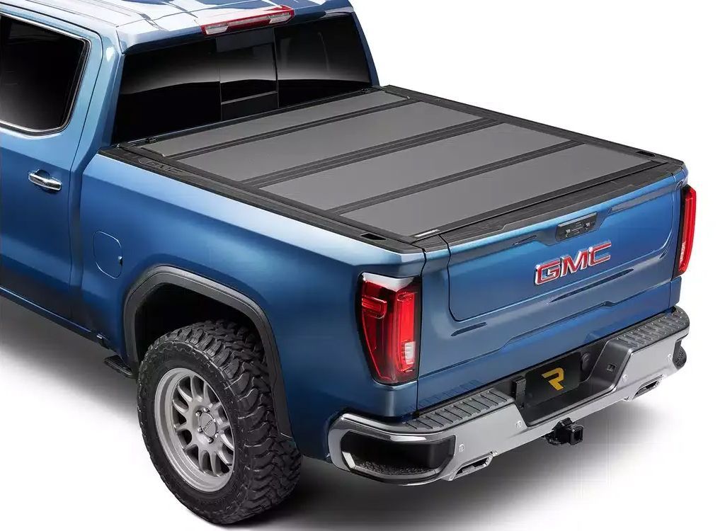 Blue pickup truck with a hard tonneau cover over the bed, shown from the rear-left side.