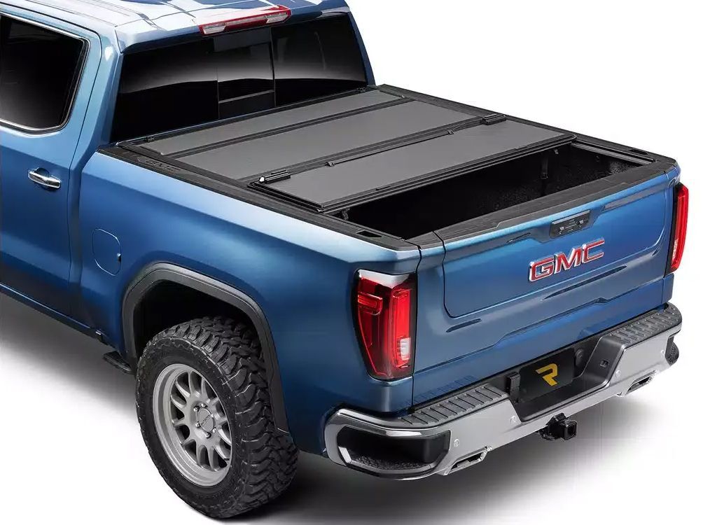 Blue GMC pickup truck with black tonneau cover, shown from the rear side view