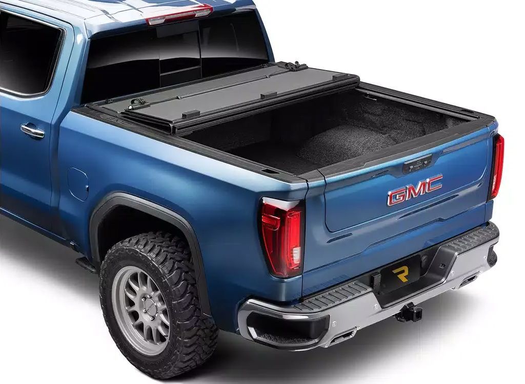 Blue GMC pickup truck with a black bed cover and open tailgate, shown from the rear three-quarter view