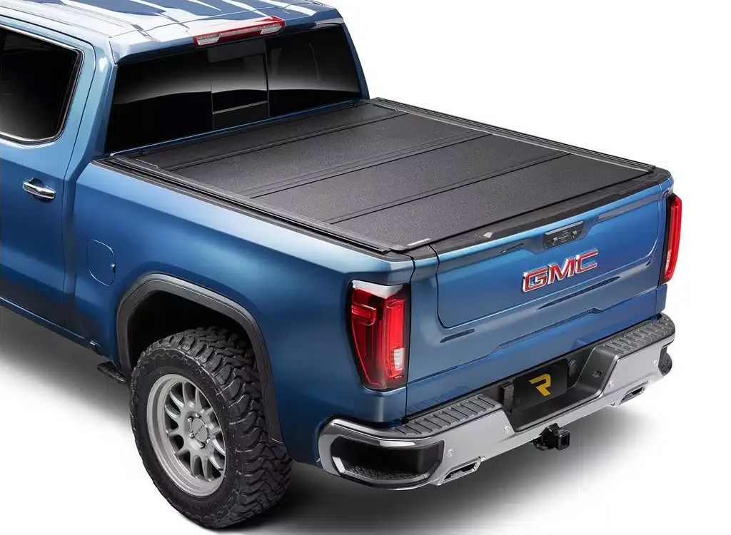Blue GMC pickup truck with a black hard tonneau cover, rear three-quarter view