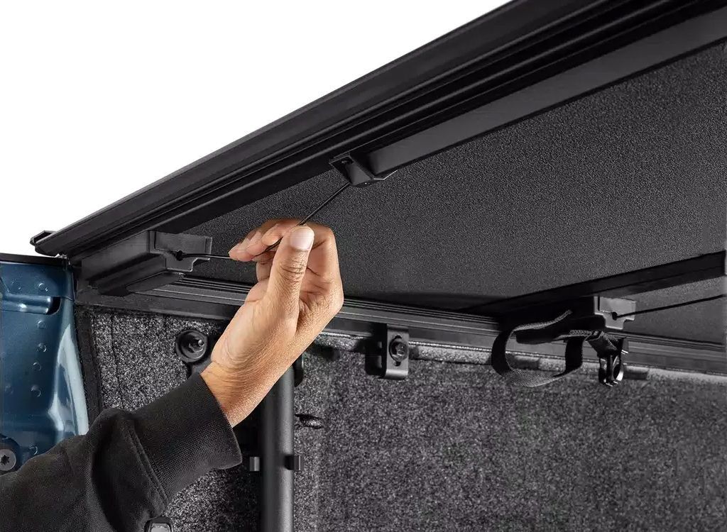 Hand adjusting a black awning or canopy mechanism on the underside of a vehicle roof.