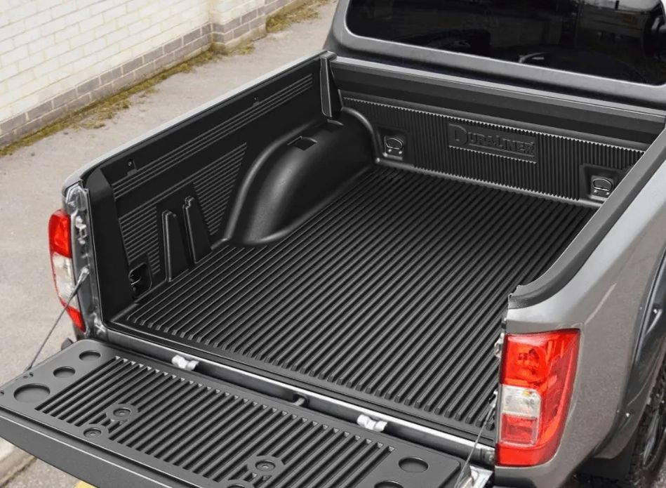 Open pickup truck bed with black ribbed liner and tailgate down, parked beside a wall