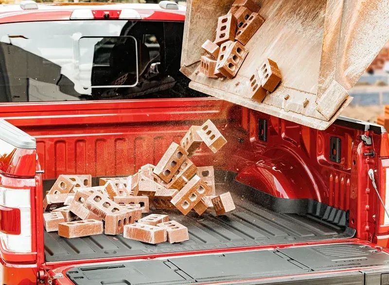 Red pickup truck bed loaded with scattered wooden bricks and a tipped crate unloading them