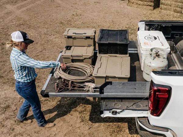 Worker loading coiled hose and gear into a white pickup truck in a dry field
