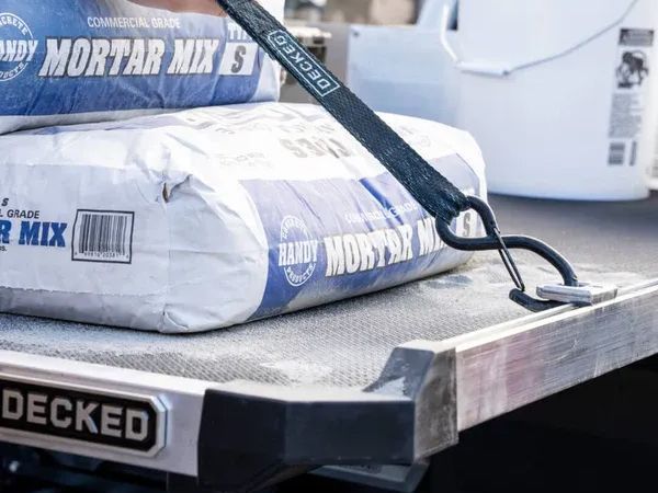 Pallet of mortar mix bags strapped on a truck bed with a shovel resting on top