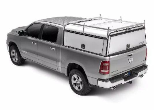 Silver pickup truck with a white utility toolbox mounted in the bed, viewed from the rear-left side