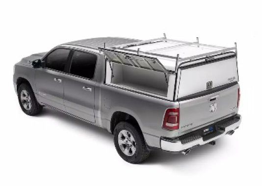 Silver pickup truck with a white camper shell, shown in a studio view from the rear side
