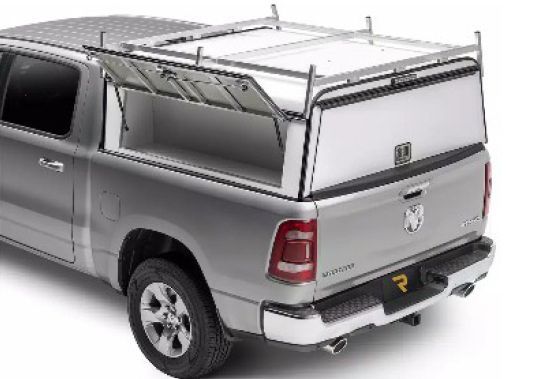 Silver pickup truck with a white utility toolbox mounted in the bed, viewed from the rear-left side