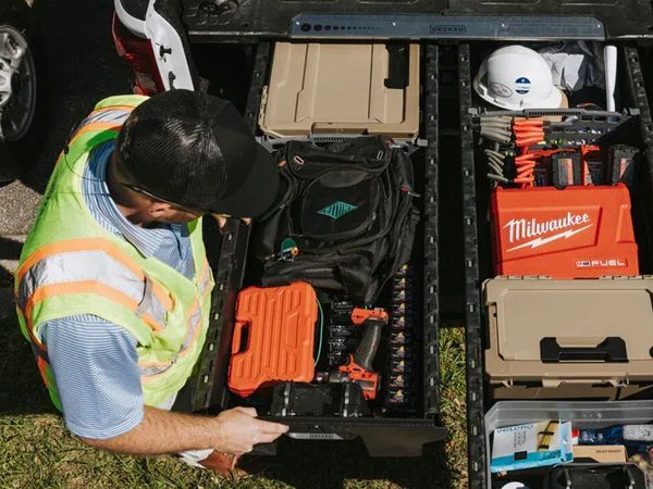Worker organizing tools in a truck bed with Milwaukee cases and orange equipment trays