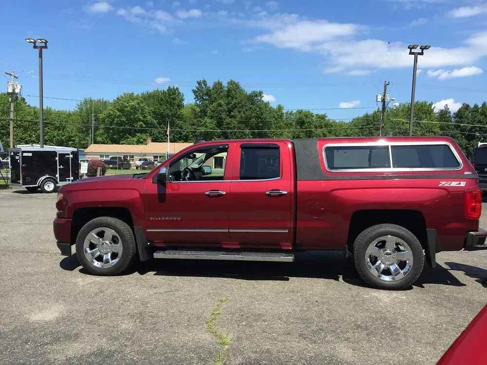 Red pickup truck with camper shell parked on pavement under a blue sky