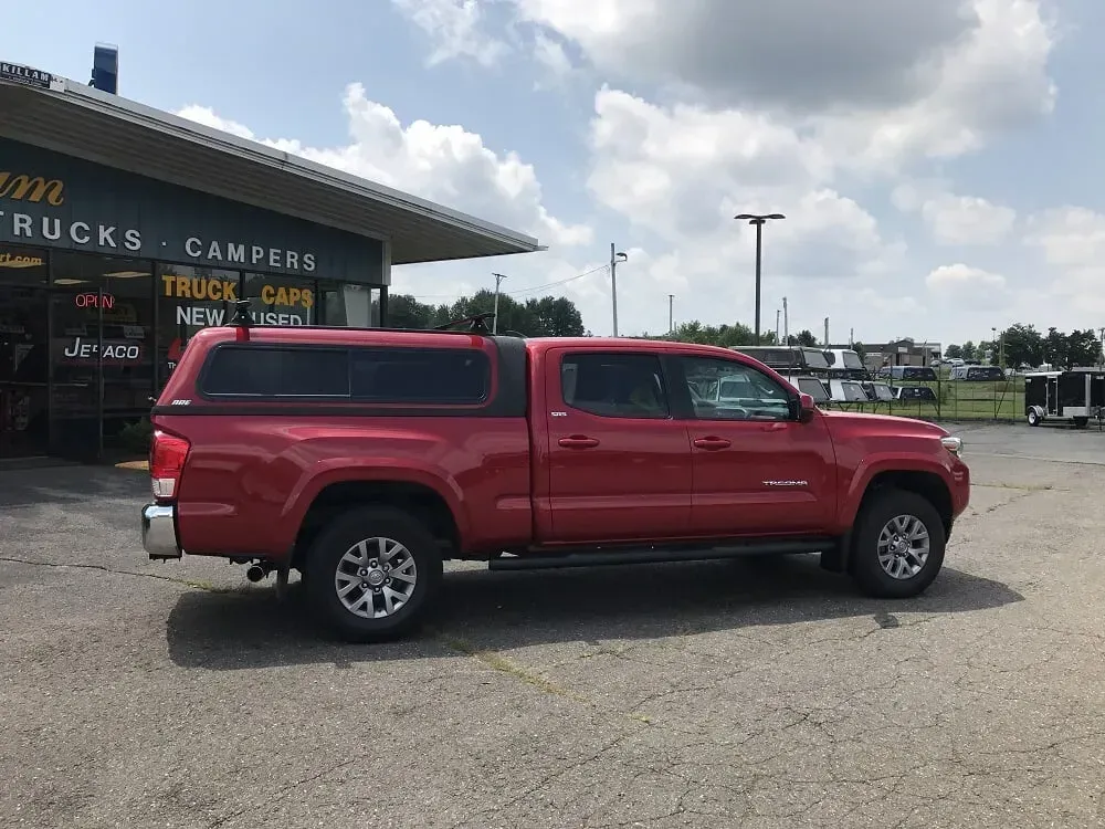 Red pickup truck parked outside a truck cap and camper shop under a partly cloudy sky