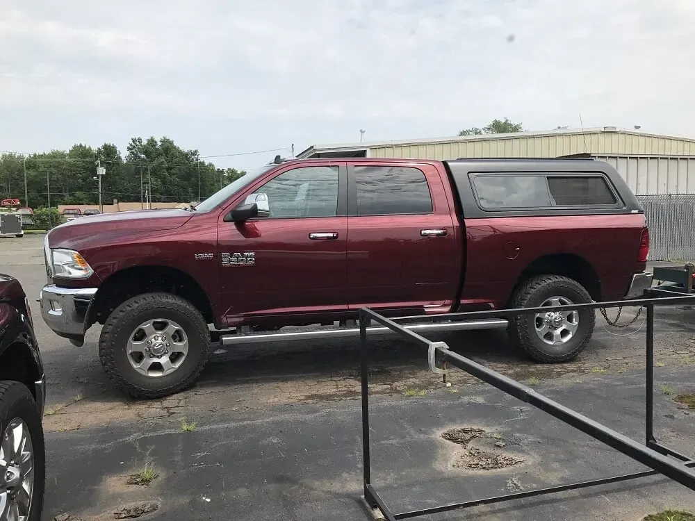Maroon pickup truck with camper shell parked in a lot behind black railings.