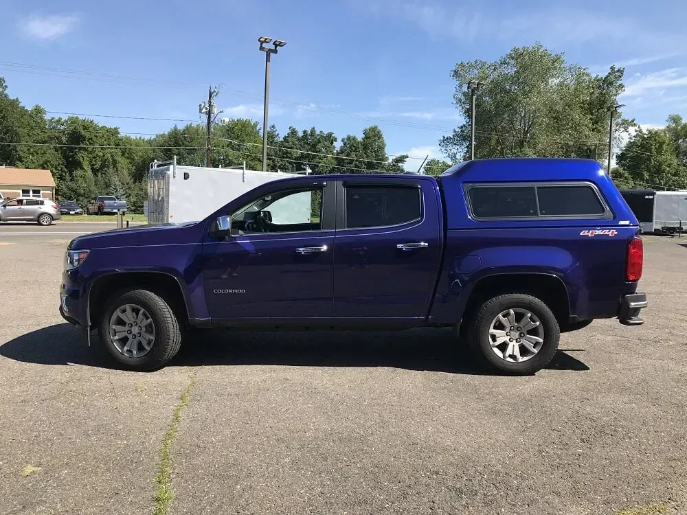 Purple pickup truck with camper shell parked in a lot under a blue sky