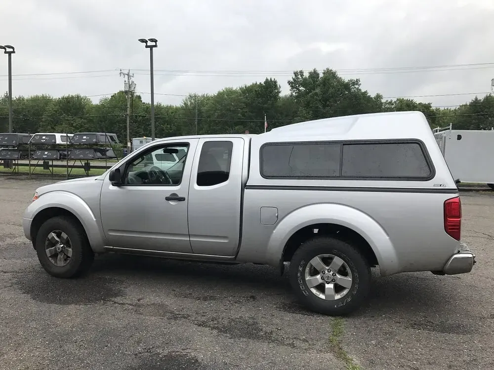 Silver pickup truck with camper shell parked on wet pavement in a lot