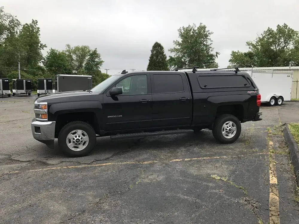 Black pickup truck with camper shell parked in a lot on an overcast day