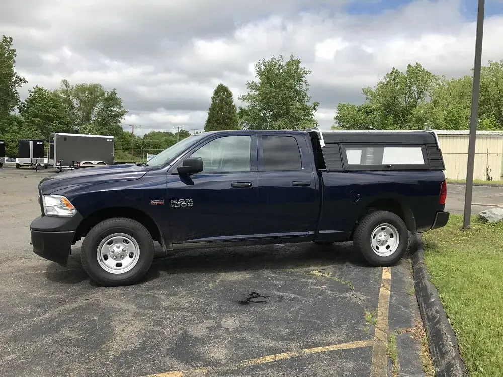 Dark blue pickup truck parked on pavement beside grass, under cloudy sky