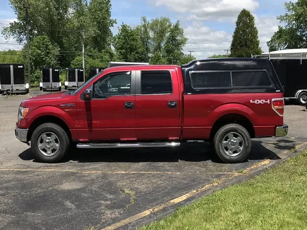 Red pickup truck parked on asphalt beside grass and trees under a cloudy sky.