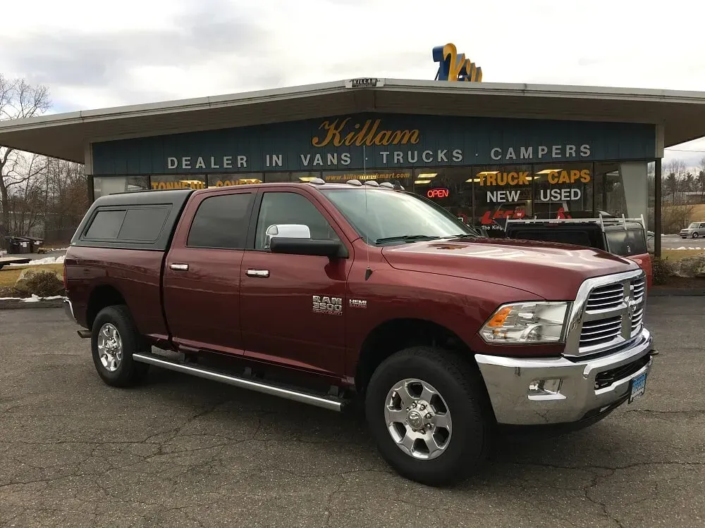 Maroon RAM pickup truck parked outside a used truck and camper dealership.