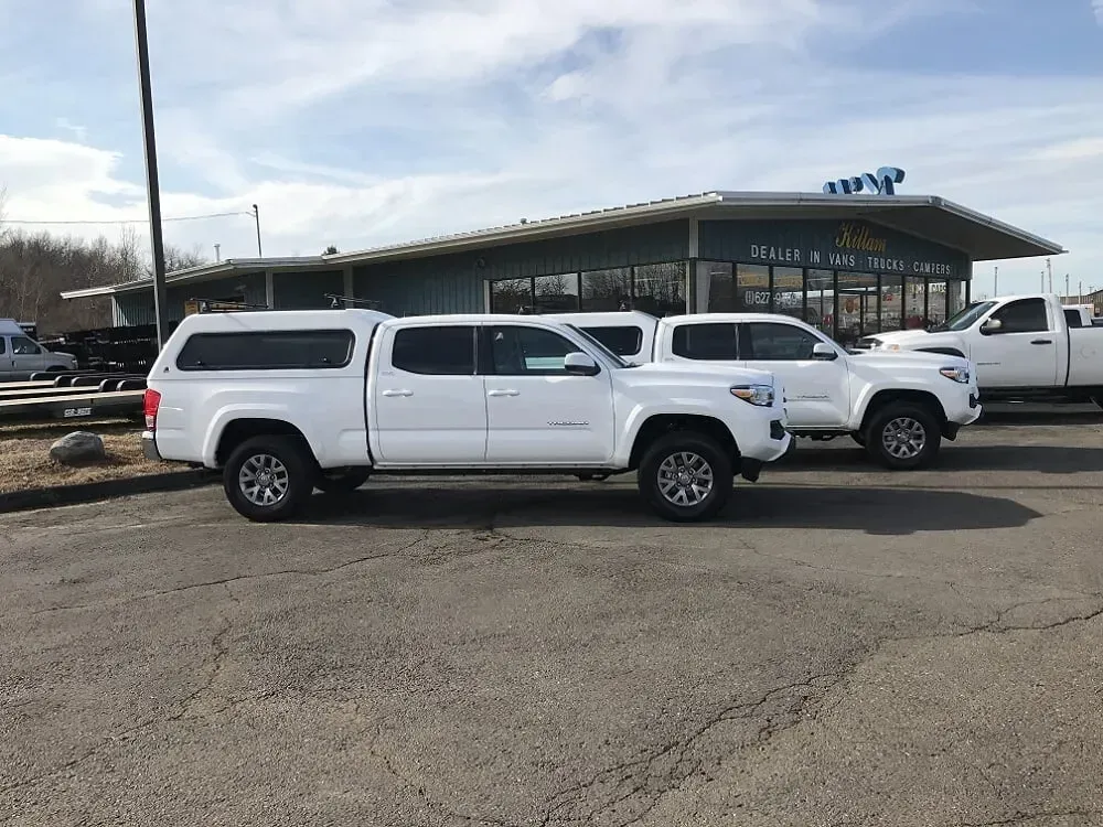 Three white pickup trucks parked outside a building on a gravel lot.