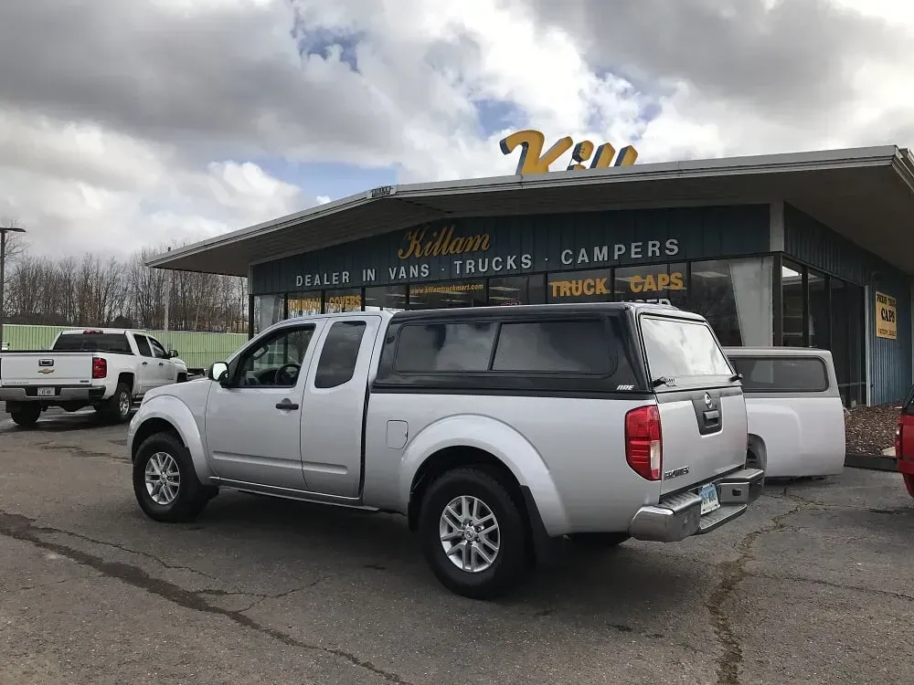 Silver pickup truck parked outside a truck accessories and camper store under cloudy skies