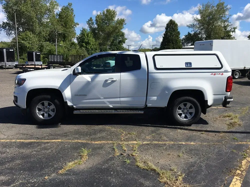 White pickup truck with camper shell parked in a lot under a sunny sky