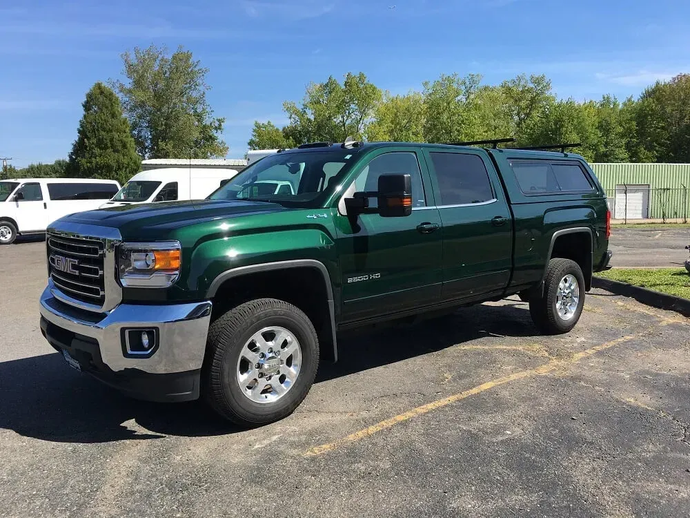Dark green pickup truck parked on a sunny lot near trees and other vehicles