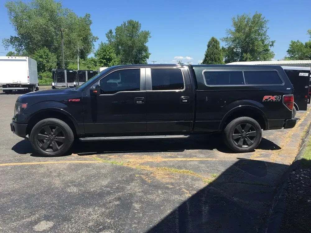 Black pickup truck with camper shell parked on a sunny lot