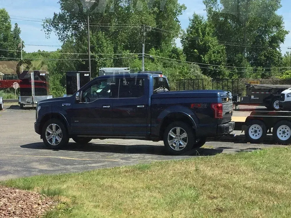 Dark blue pickup truck towing a trailer on a paved lot, with trees and grass in the background