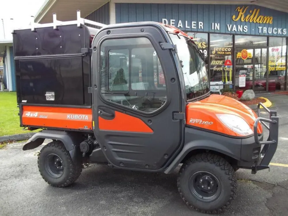 Orange and black mini dump truck parked outside a van dealership