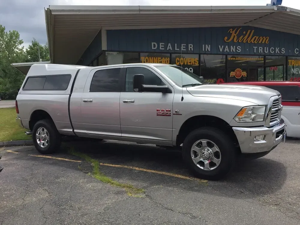 Silver RAM pickup truck with camper shell parked outside a dealership building.