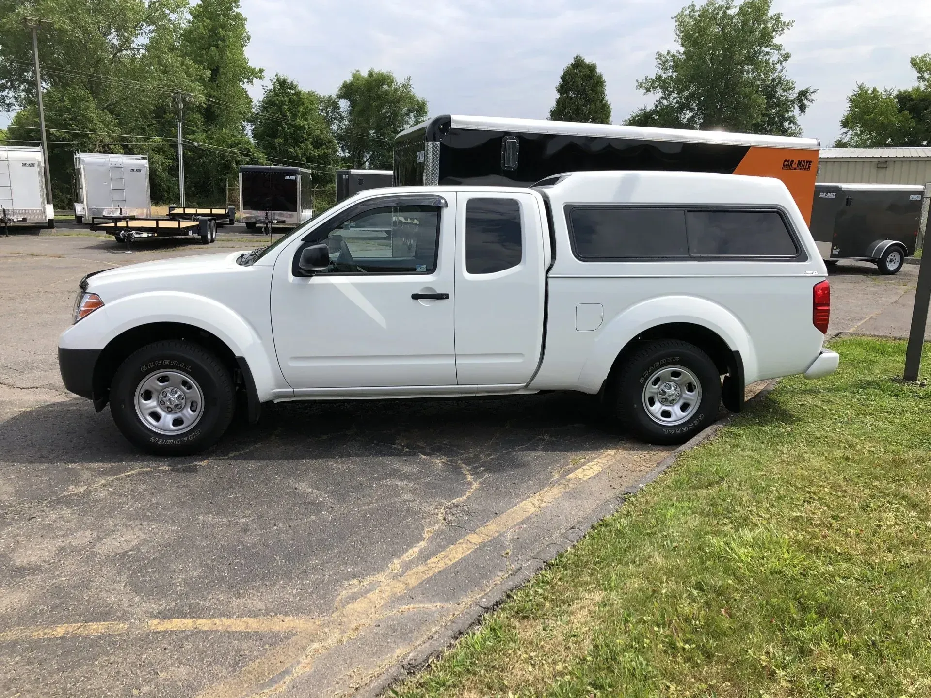White pickup truck with camper shell parked on a paved lot near grass and trees