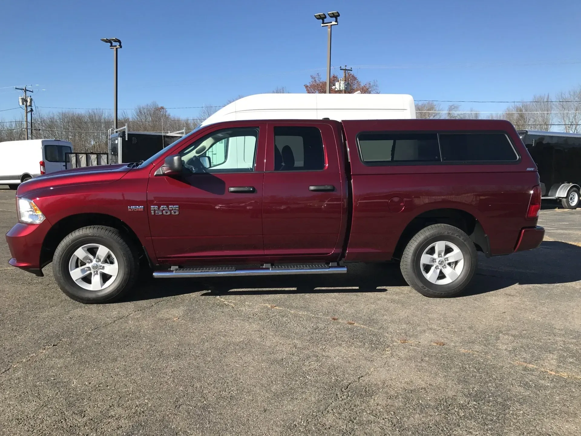 Maroon pickup truck with a white camper shell parked on a gravel lot under a clear sky