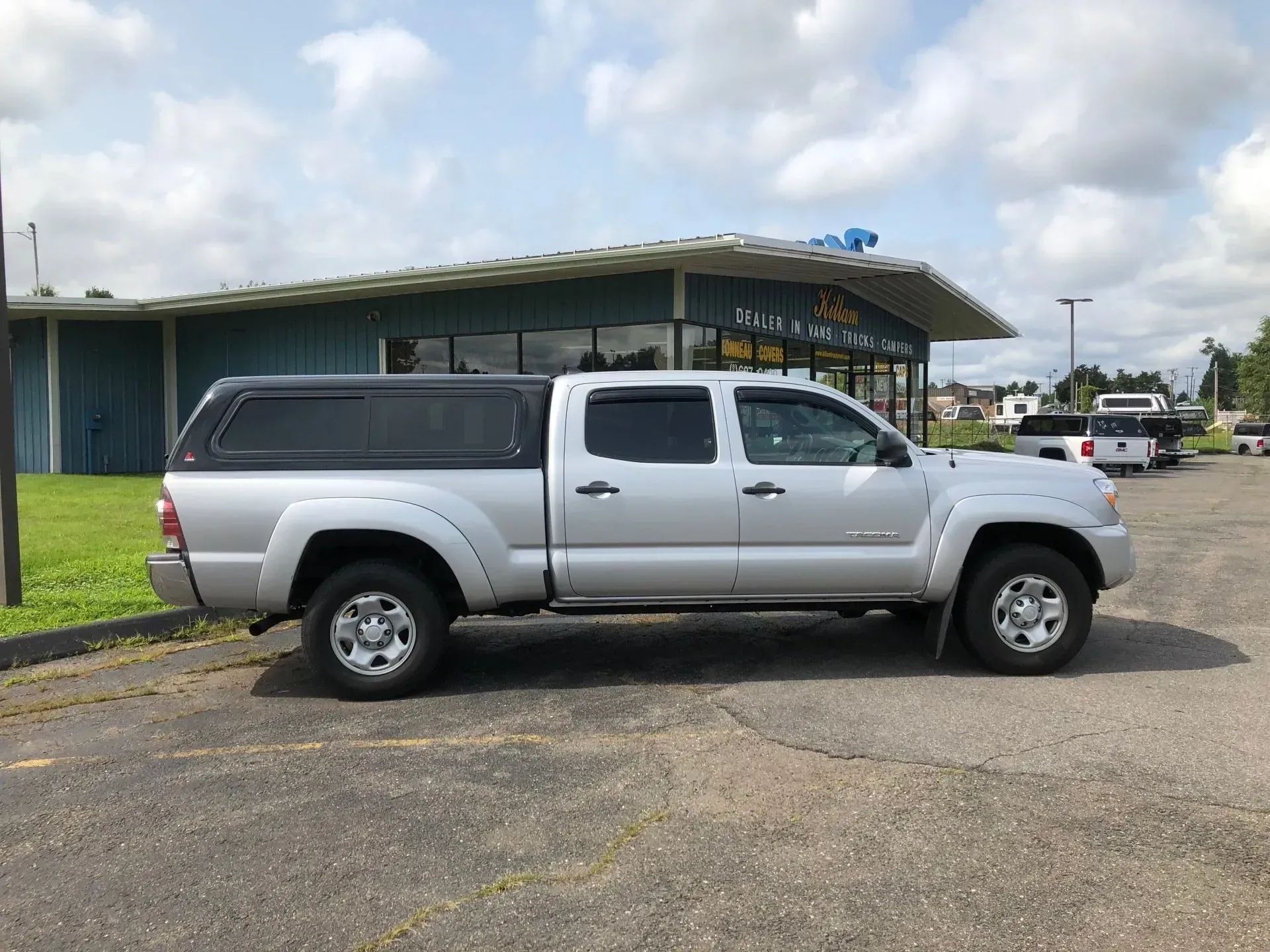 Silver pickup truck parked beside a green building under a cloudy sky.