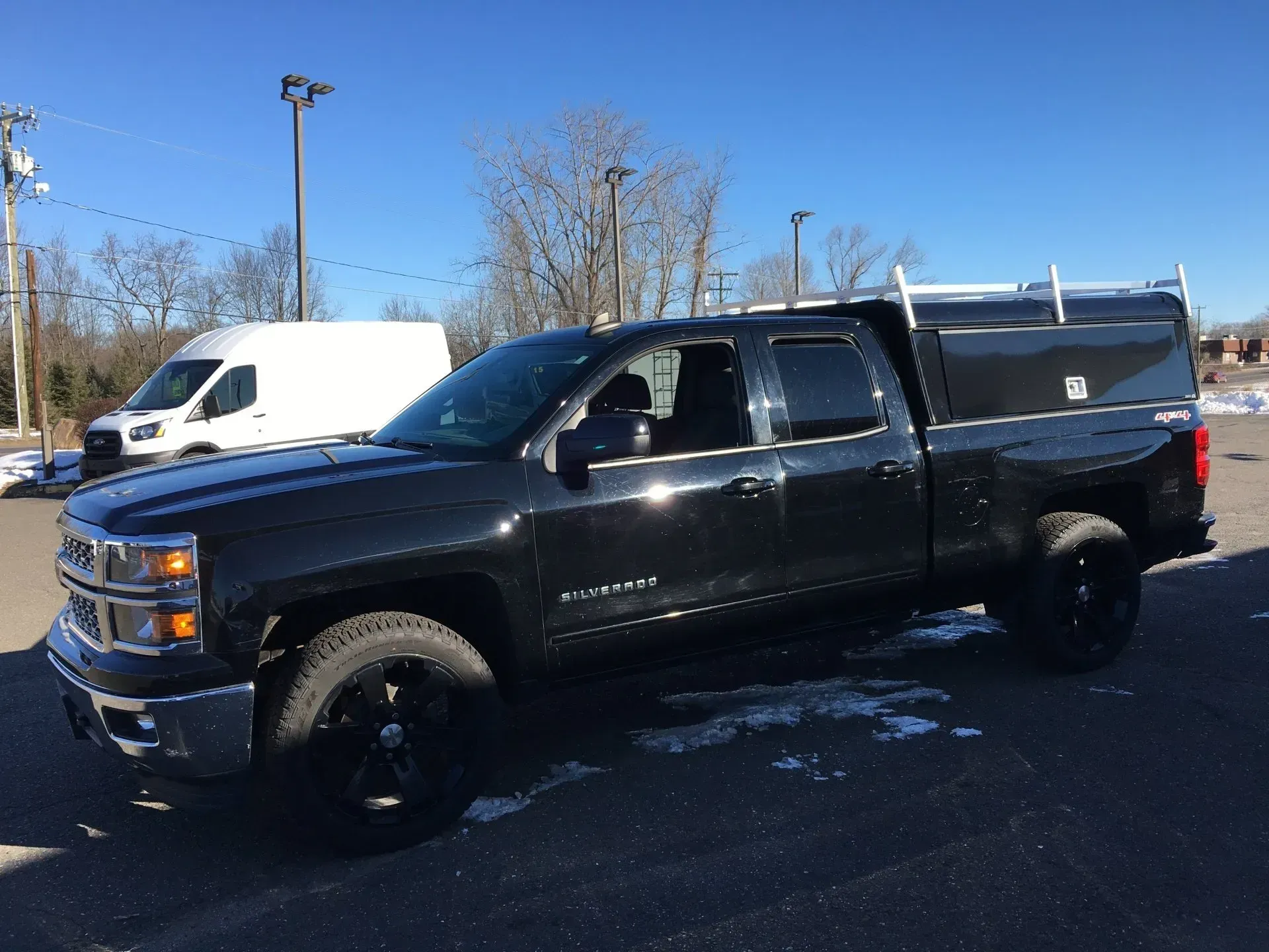 Black pickup truck parked in a sunny lot with a white van in the background