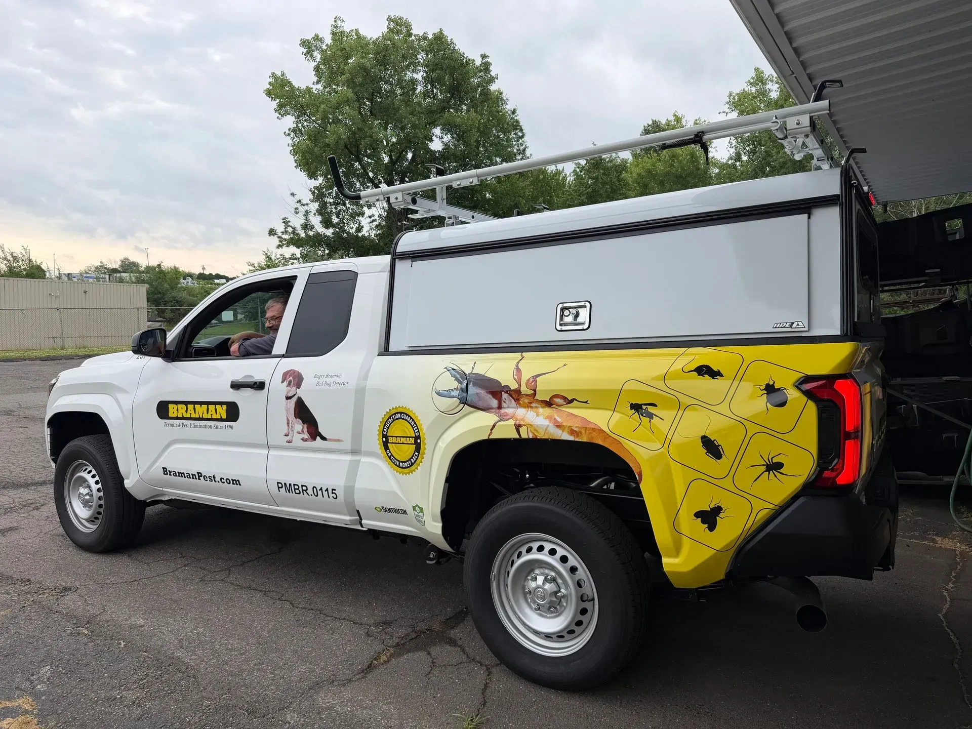 White utility truck with yellow rear graphics and roof rack parked outdoors under an overcast sky