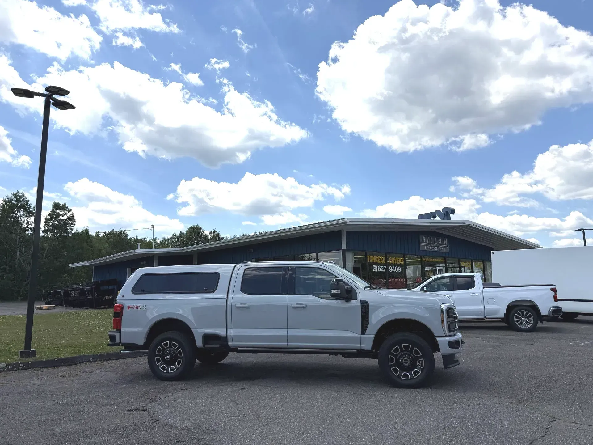 Two lifted pickup trucks parked outside a low building under a cloudy sky