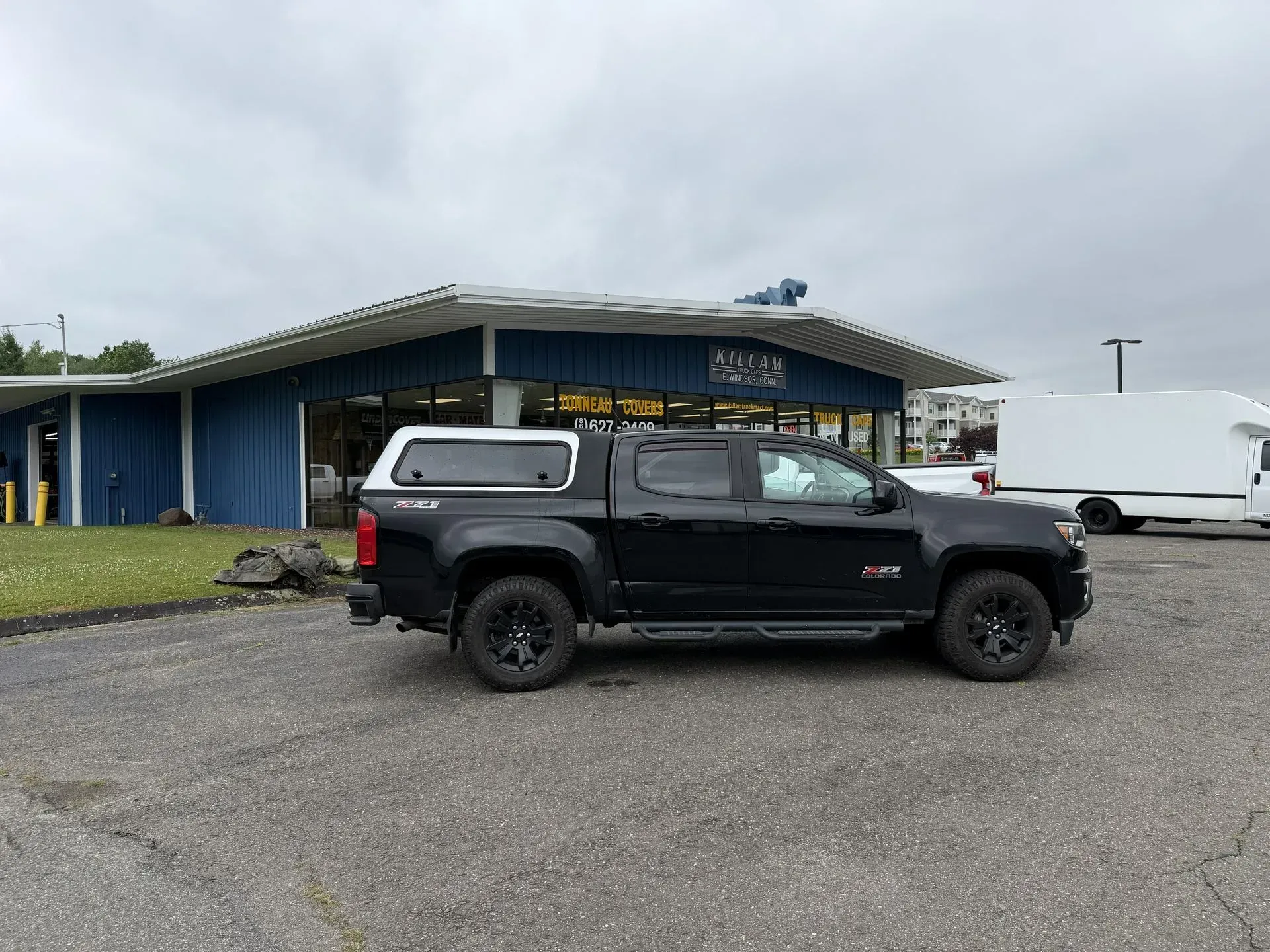 Black pickup truck parked in front of a blue building on an overcast day