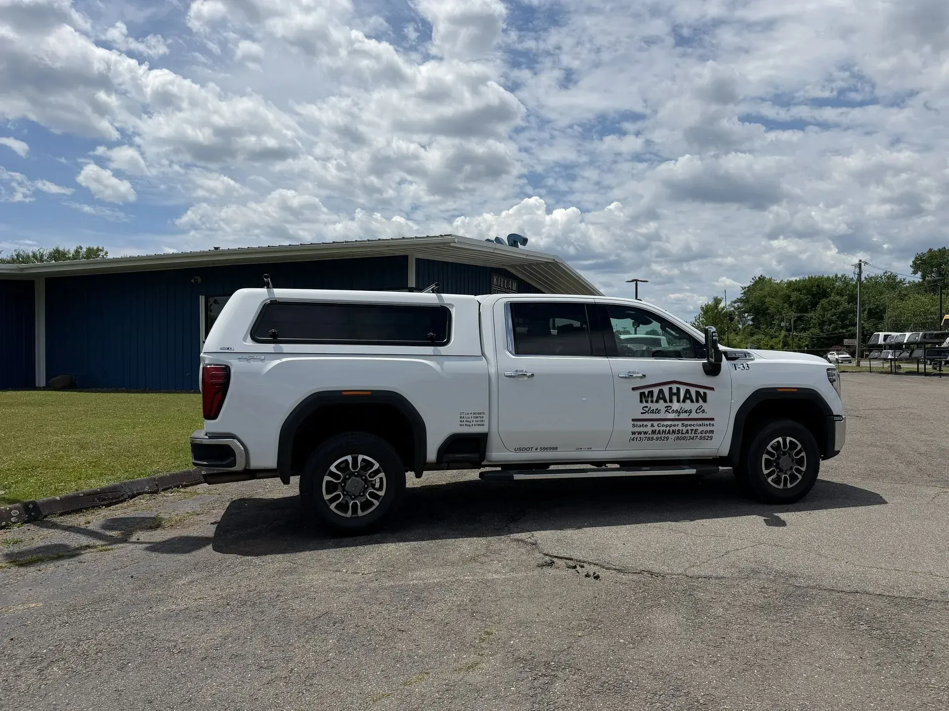 White utility pickup truck parked on a paved lot under a cloudy sky, with logo on the side