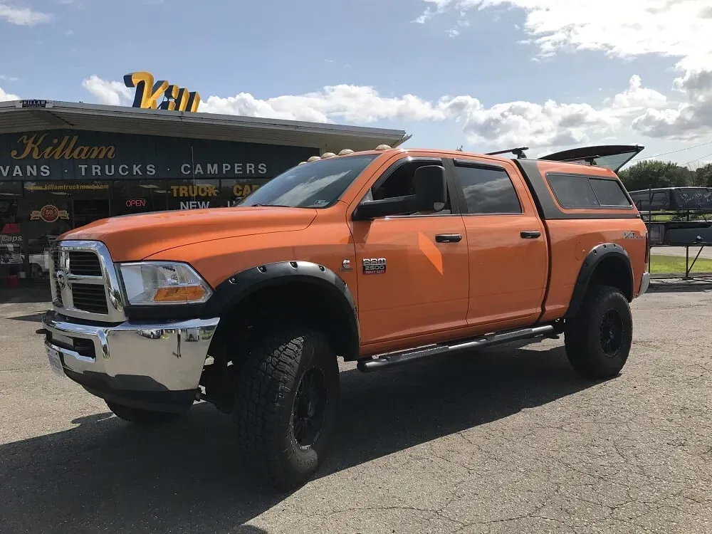 Orange pickup truck with camper shell parked outdoors on a sunny lot