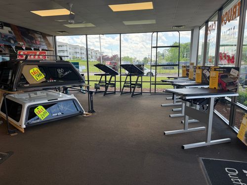 Retail store interior with display tables, bright windowed storefront, and sale signs on carpeted floor