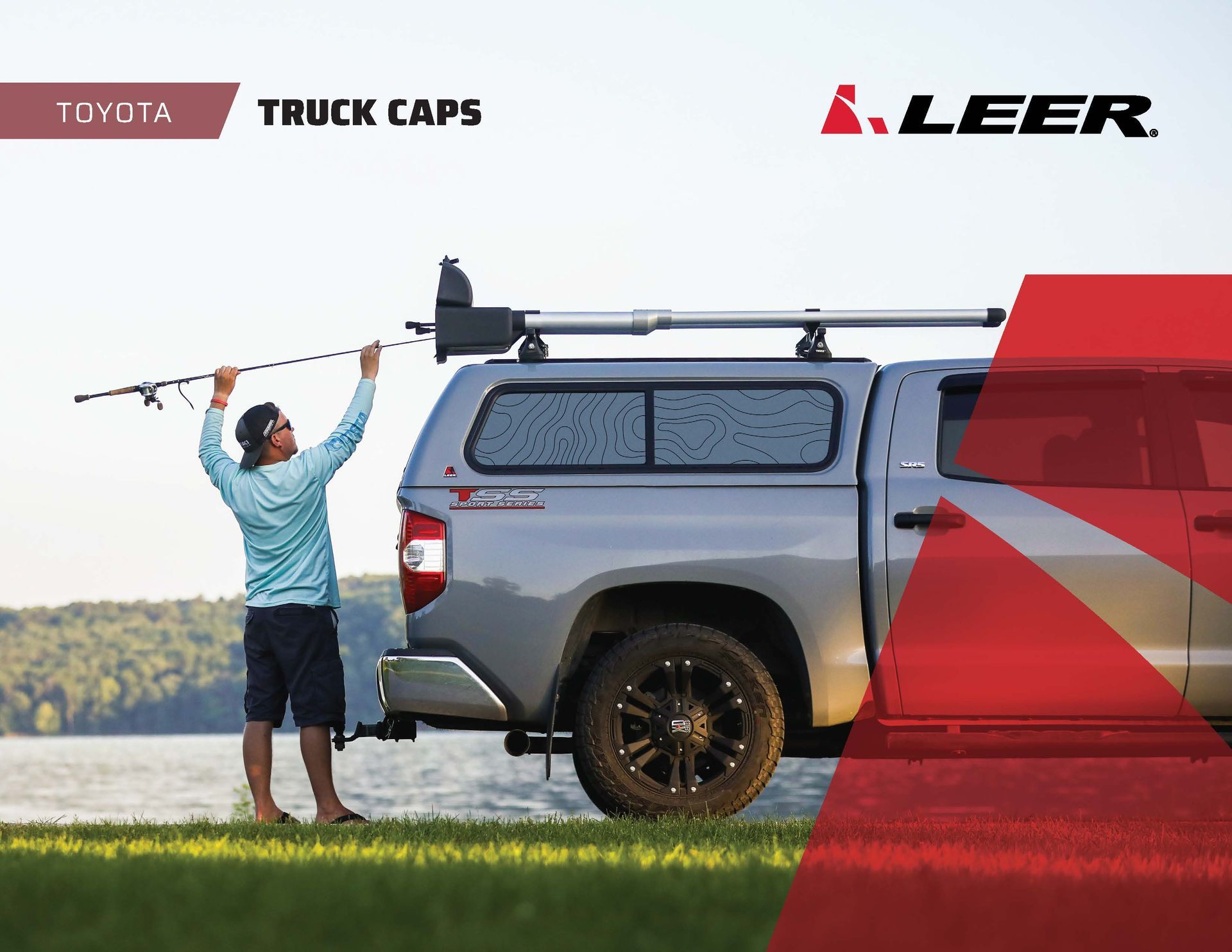 Person loading fishing gear beside a silver Toyota truck with a LEER truck cap on a lakeside road