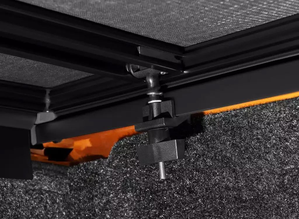 Black metal hinge or bracket attached under a textured surface with an orange component and a visible bolt