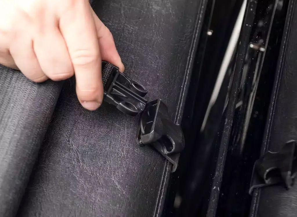 Hand fastening a black car seatbelt buckle near a gray fabric seat.